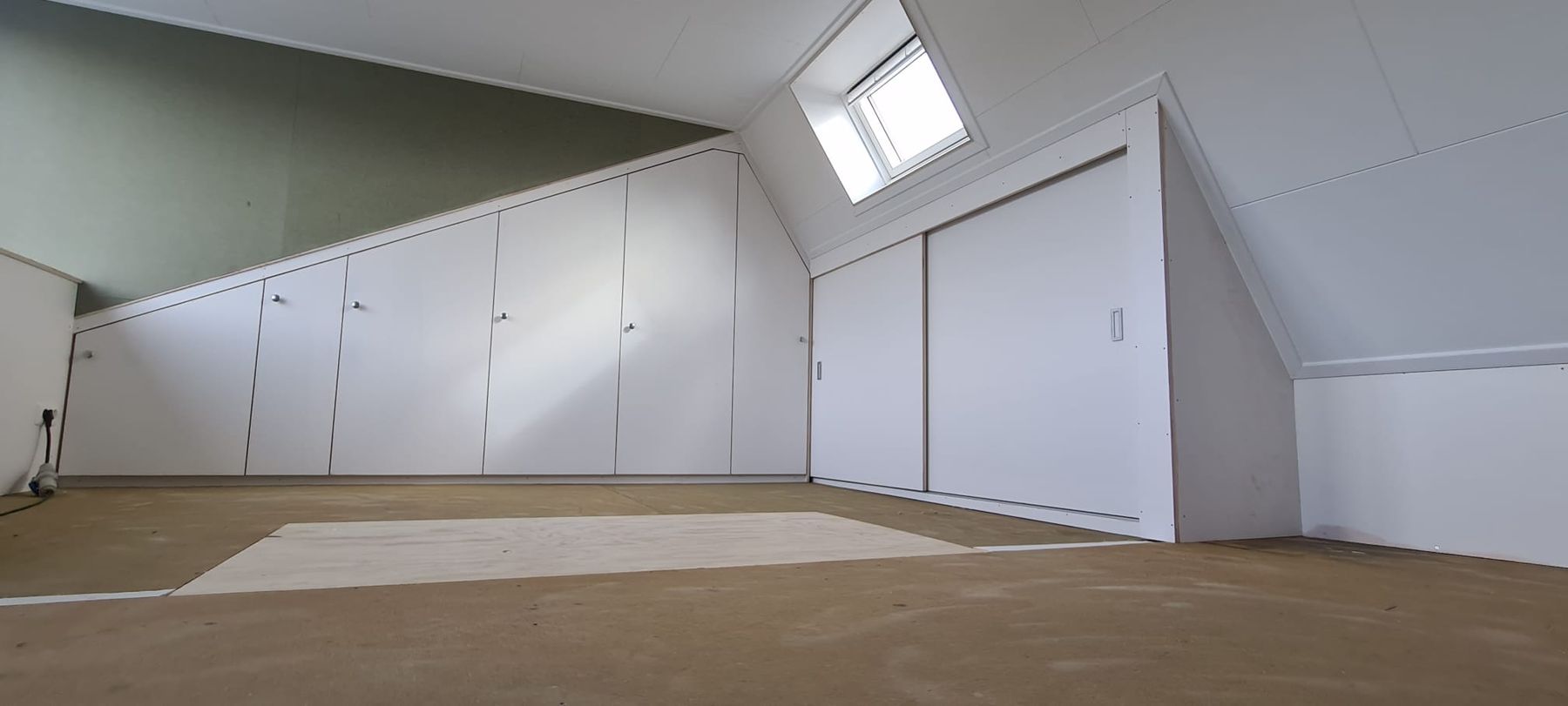Afgewerkte zolder met witte inbouwkasten onder het schuine dak