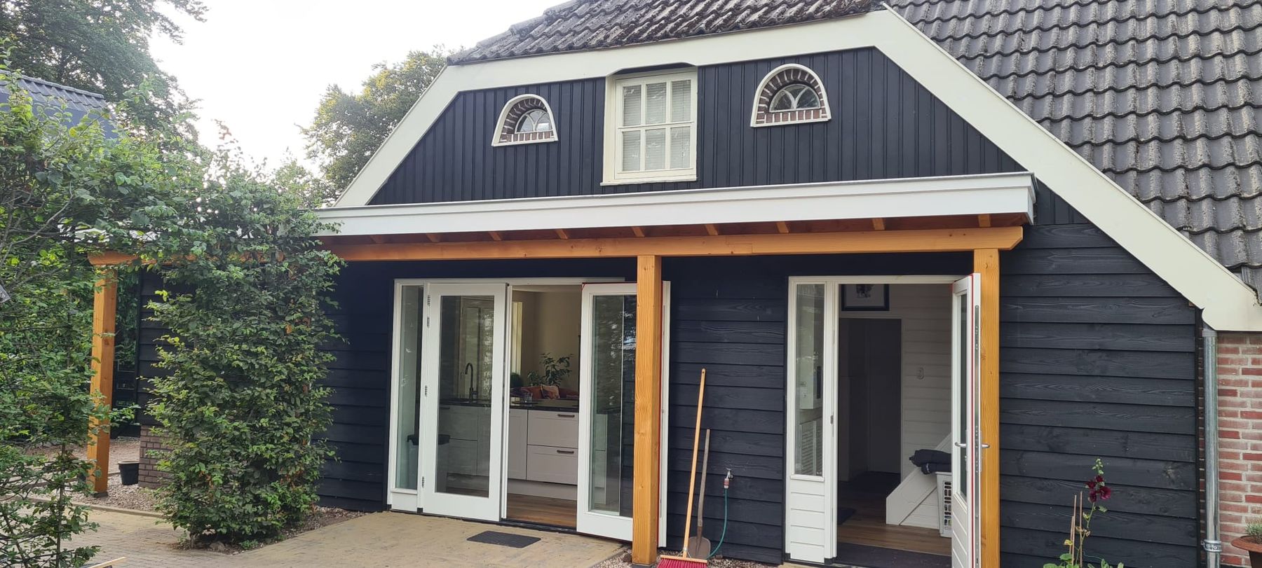 Aanbouw met zwarte houten gevelbekleding, witte kozijnen en openslaande deuren